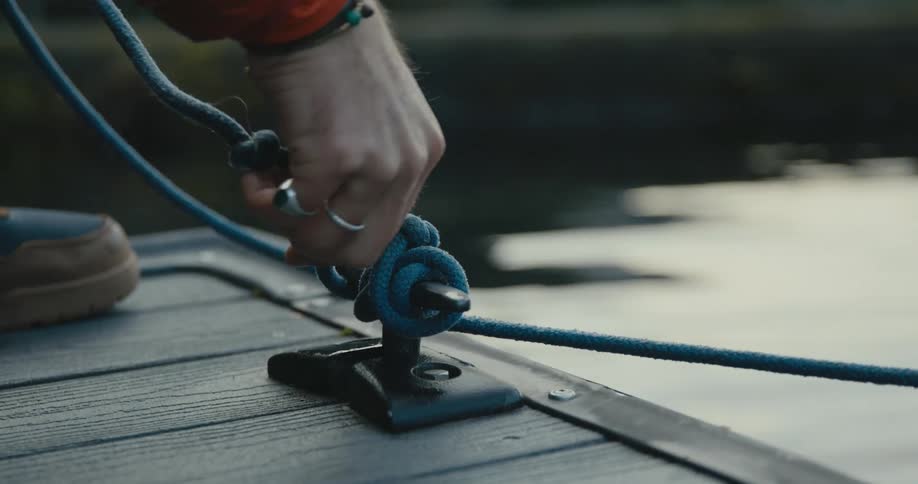 A person ties a mooring line to a cleat on a wooden pier