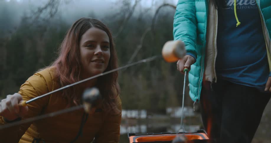 A woman smiles as she roasts a marshmallow over a campfire with friends