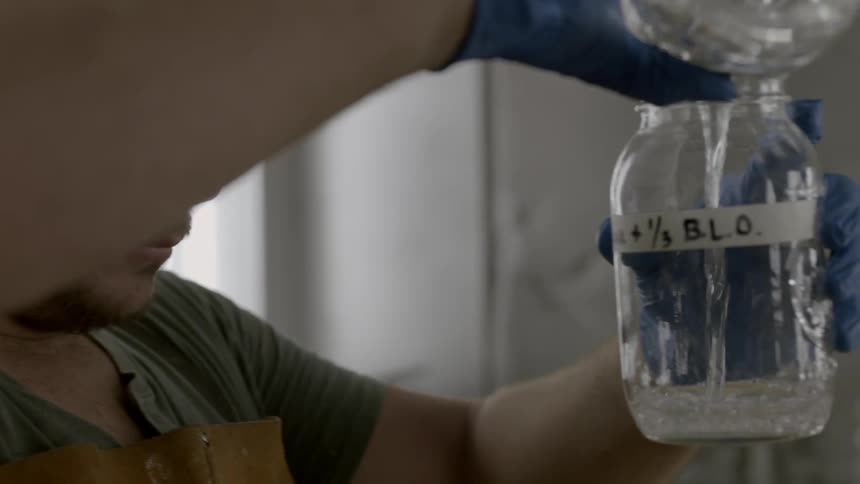A man pours liquid into another jar wearing protective gear