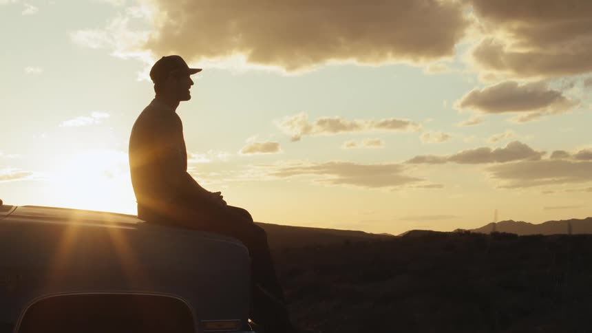 A man sits on his vehicle watching the sunset