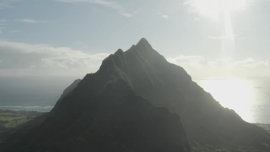 The sun shines brightly on a mountain ridge under a cloudy sky