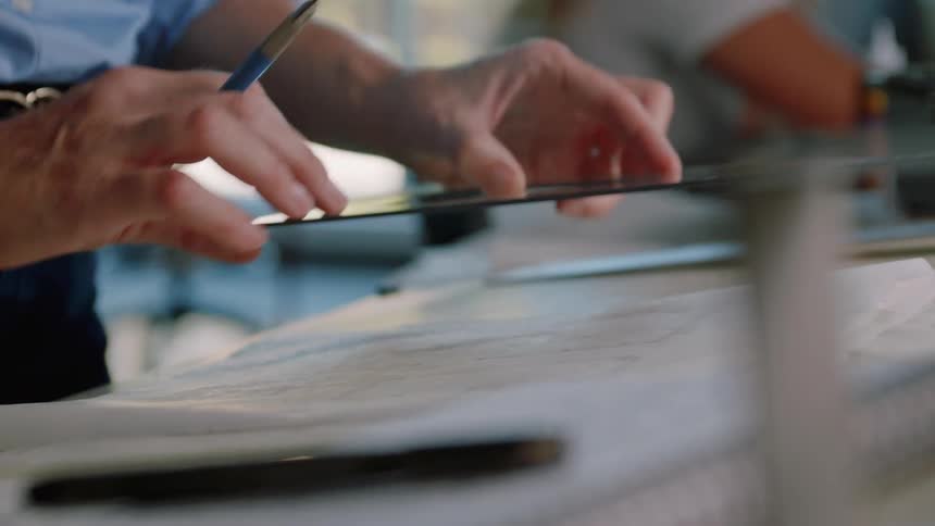 A man is holding a pen and placing a plastic triangle on a paper on the desk