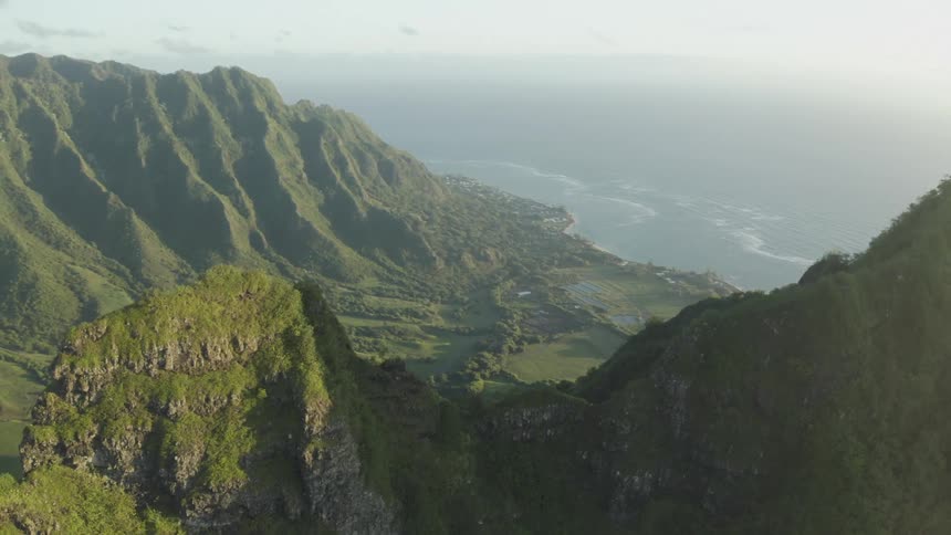 The sun shines brightly upon a mountain ridge and valley covered with green grass and plants along the coast under a foggy sky
