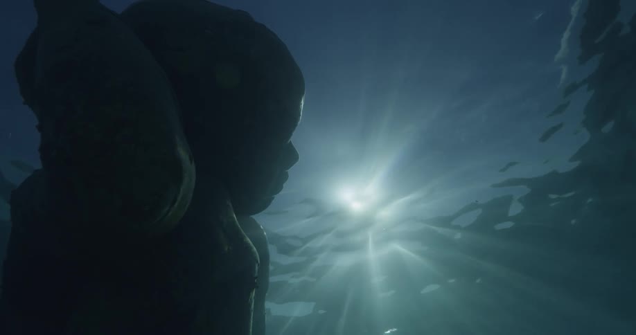 The sun shines on statue of man underwater
