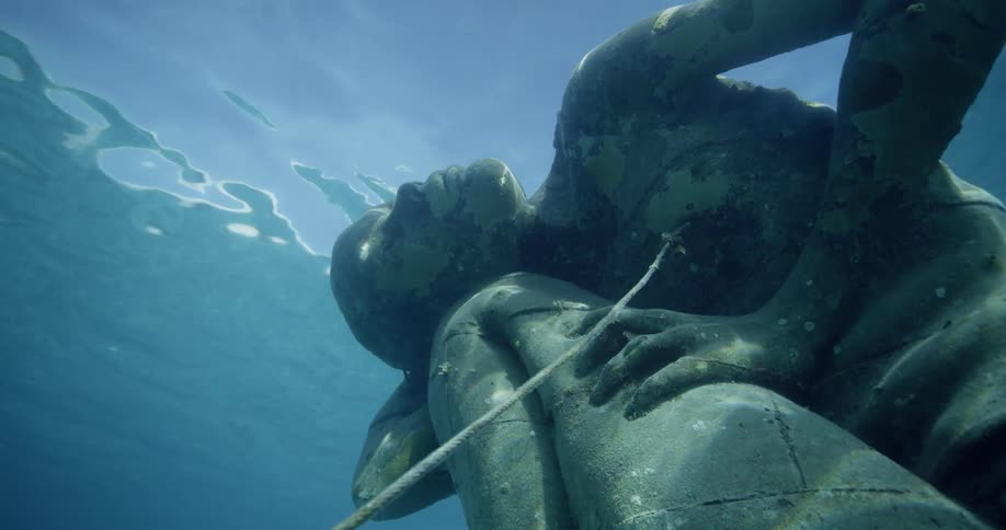 The sun shines on stone statue of man underwater