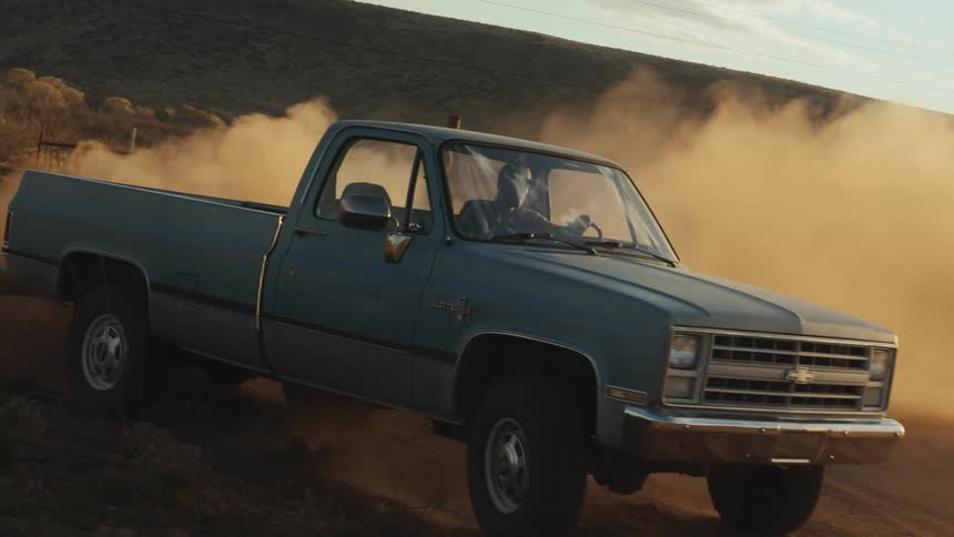 A man in a truck spins around a corner on a dirt road and creates a large dust cloud