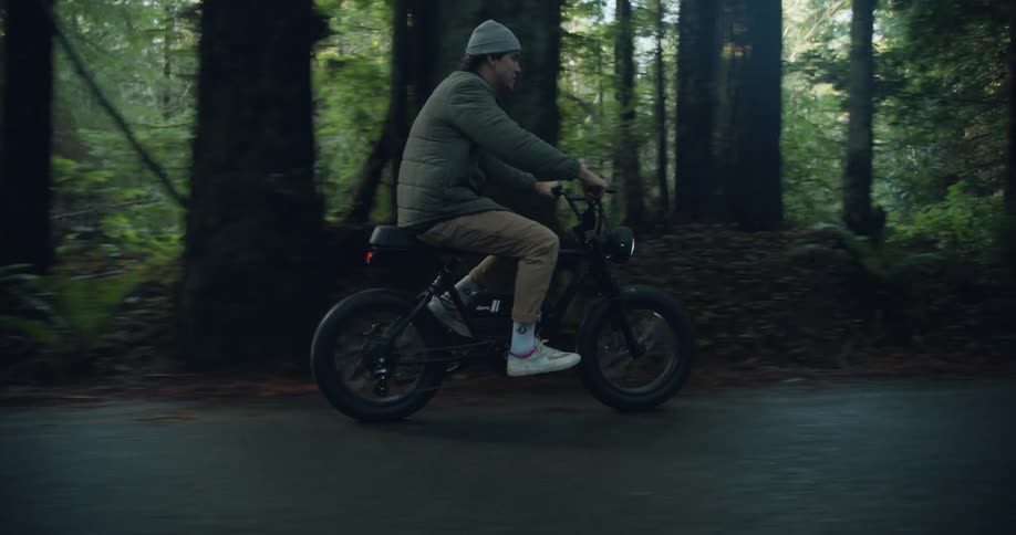 A man is riding a moped on a forest road and he takes a short leap with the bike