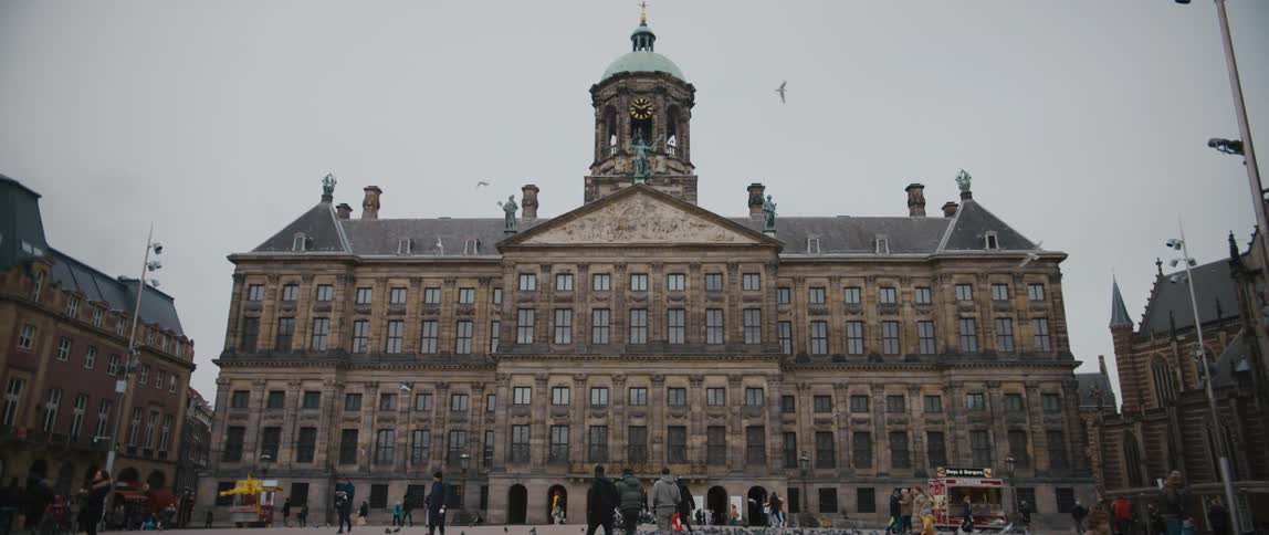 People walk in front of The Amsterdam Royal Palace as birds fly past