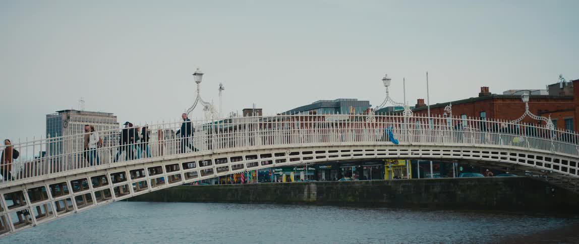 Pedestrians walking across white arched bridge over a channel of water