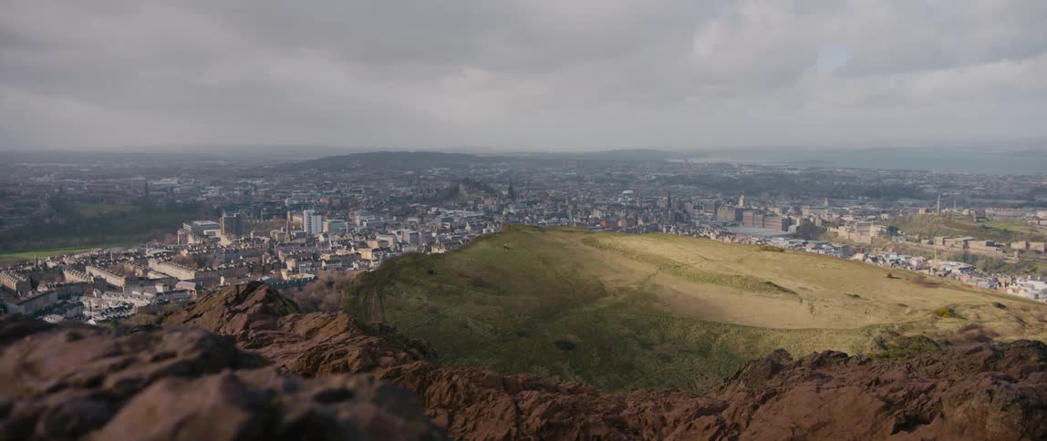View of Edinburgh, Scotland in the valley below from a grassy and rocky hill
