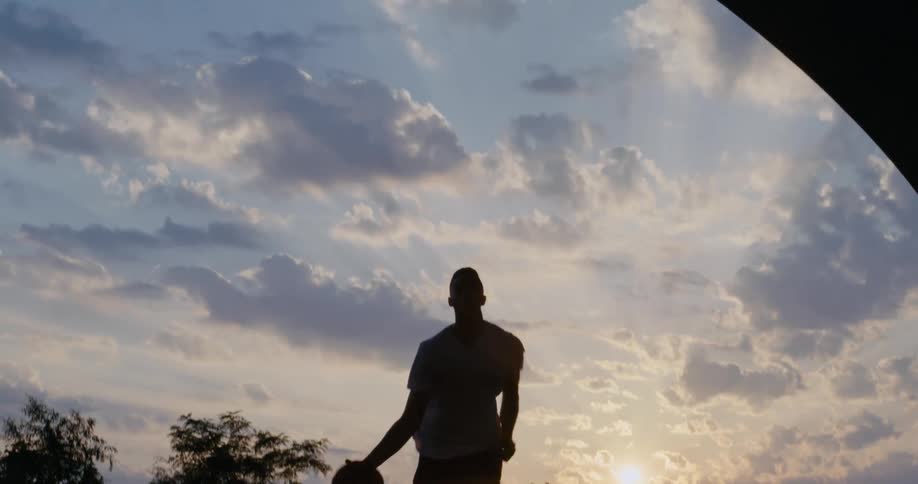 A man dribbles across an outdoor basketball court and dunks a basketball in the hoop
