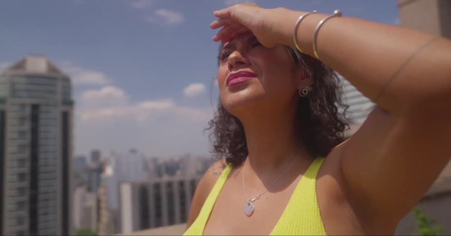 A woman shielding her eyes from the sun while standing on a rooftop in a city