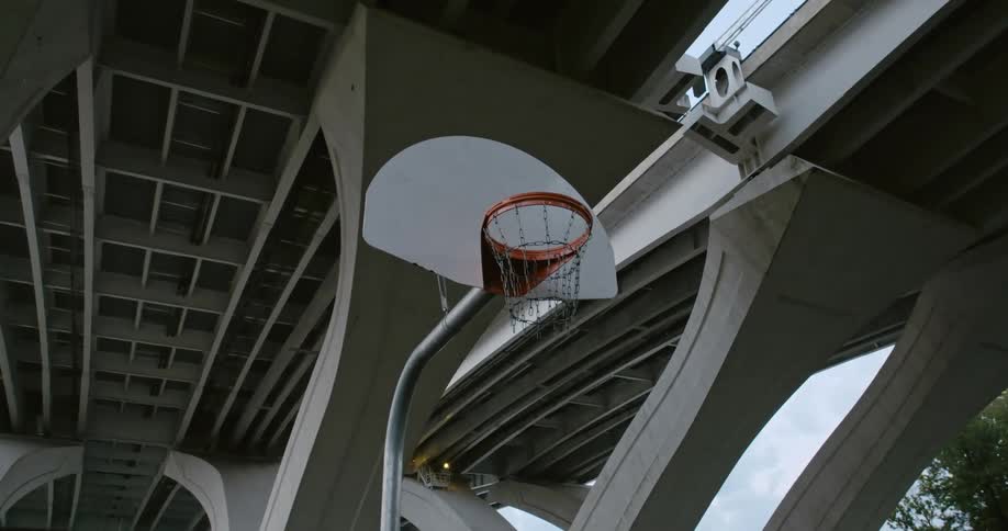 A basketball hoop sits under a bridge in the park