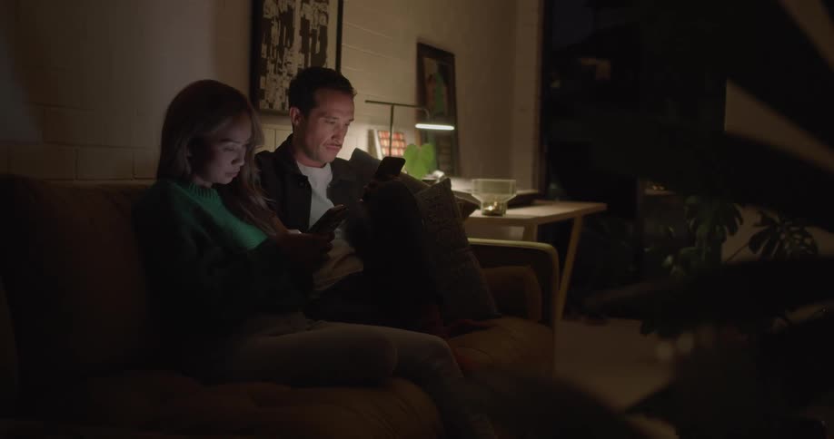 A couple scroll through their smartphones while sitting on the couch together