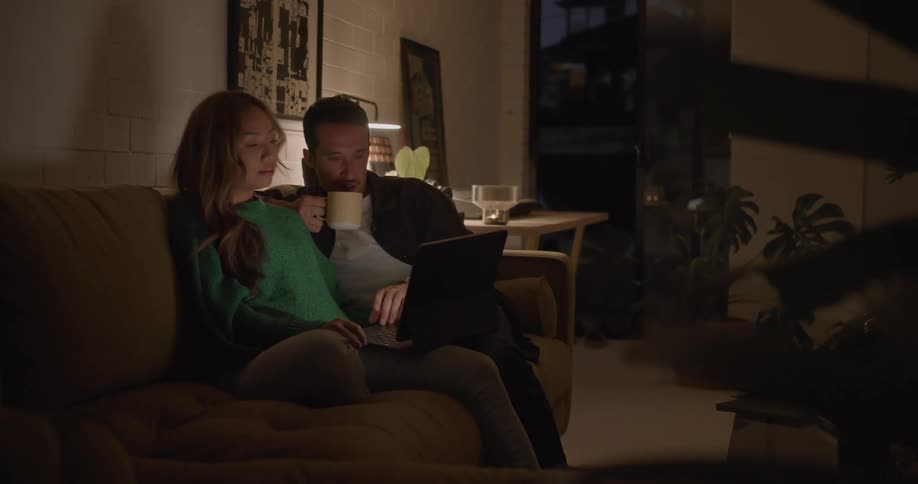 A man and woman looking at a laptop while sitting close together on a living room sofa