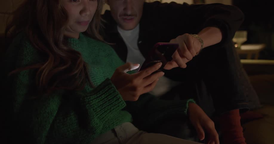Man and woman smile as the man scrolls on a cellphone that the woman is holding