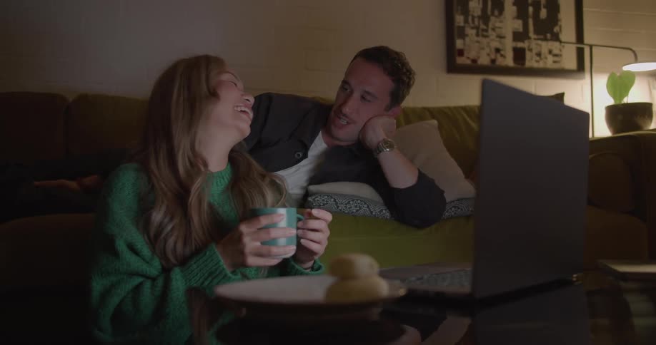 A couple laugh while watching videos on a laptop