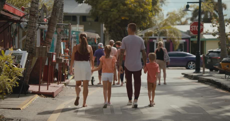 A man and woman point and walk past shops in a town as they hold hands with their children