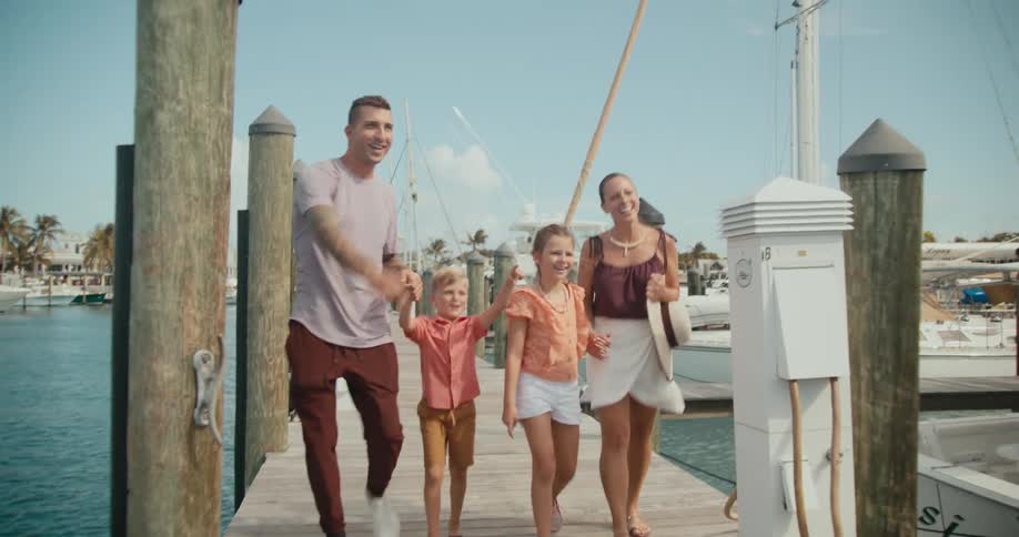 A family holds hands as they walk along a pier past boats docked in the water