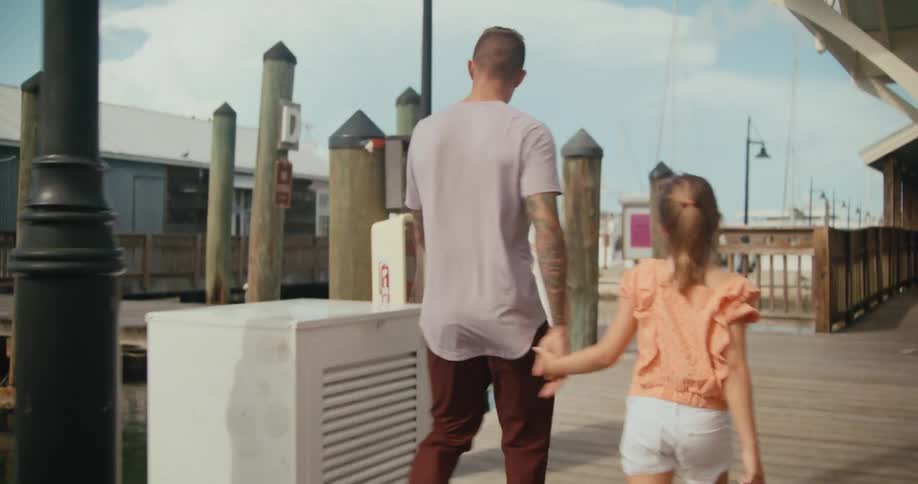 Father and daughter holding hands and walking down a wooden pier at a sunny day