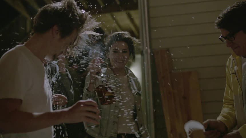 Person drinking from a can as they are being sprayed with beer from a bottle