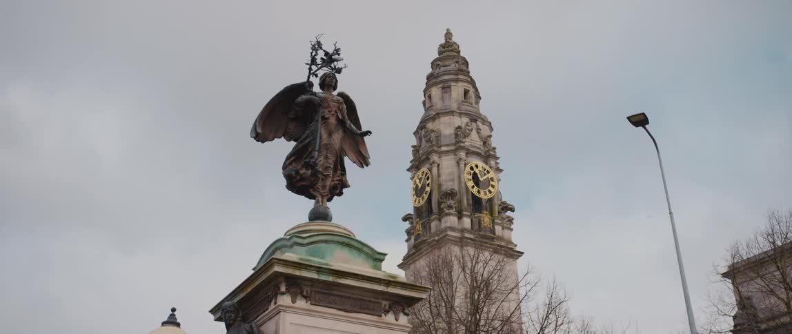 Carved clock tower stands over statue of angel and nearby streetlight
