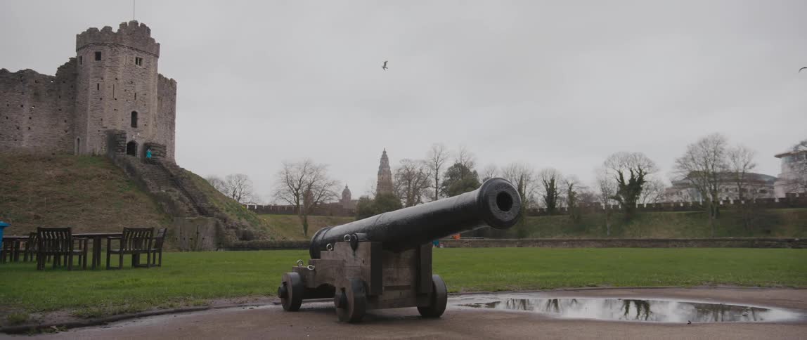 A bird flies over a castle with a canon monument out front
