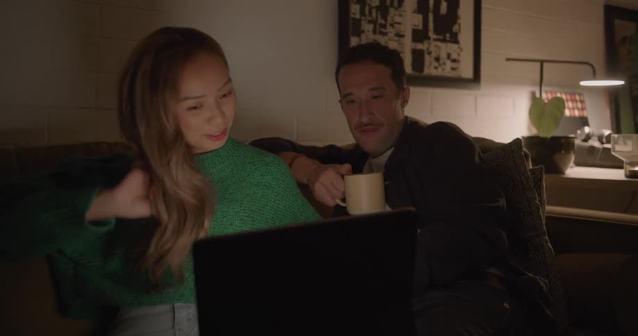 A man and woman cuddle on the couch while watching videos on a laptop