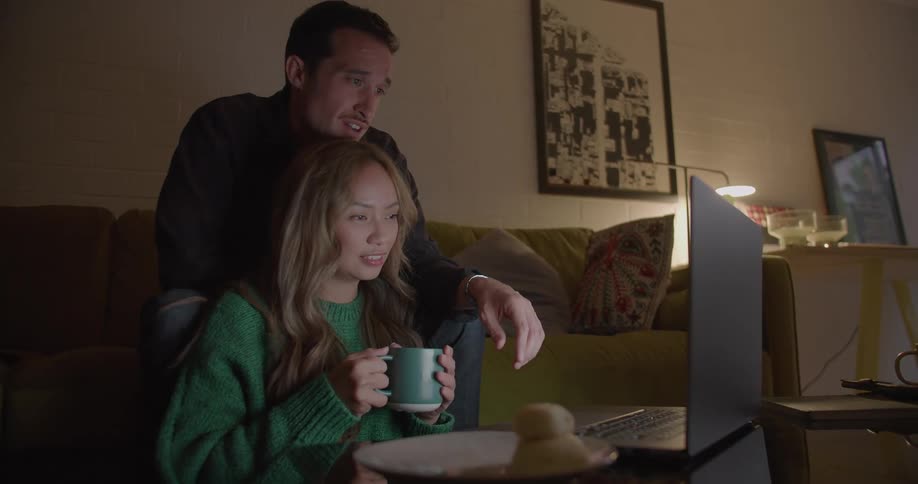 A woman rests her head on her partners leg while watching video on a laptop