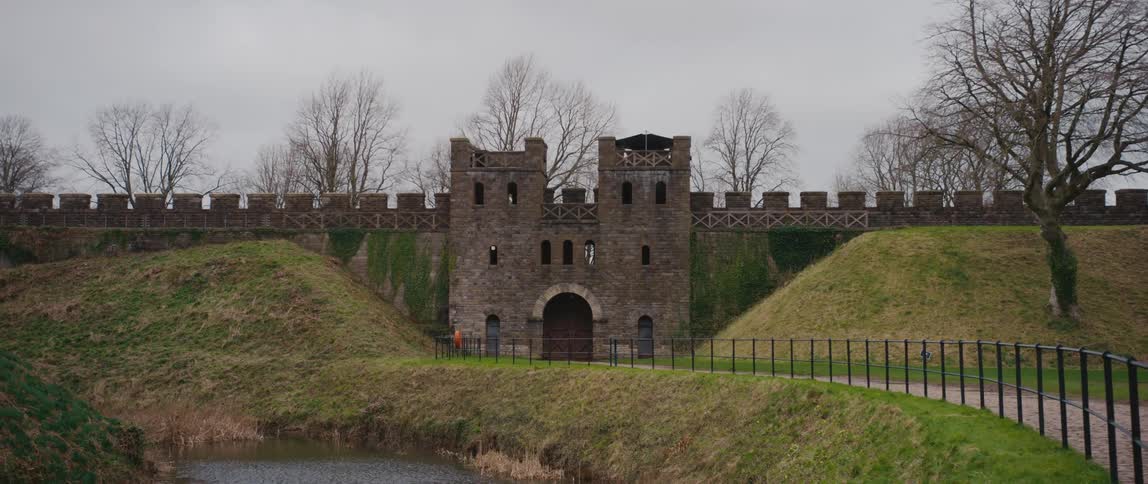 A gate to the cardiff castle in wales with fenced walkway and grassy mounds