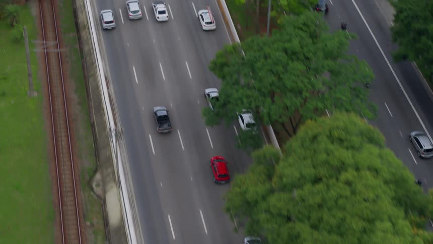An aerial view of vehicles driving past a train going in to a downtown area alongside a river