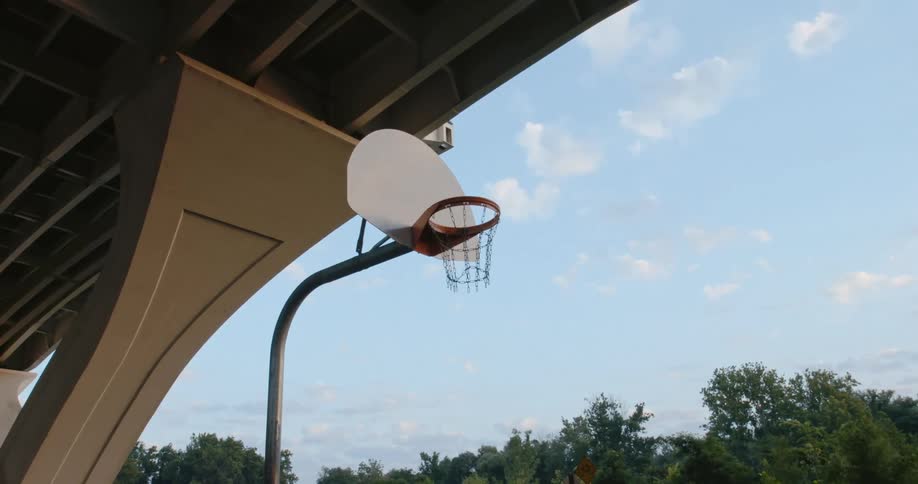 Basketball hoop and net sit under the overhang of a building near a forest under a blue sky