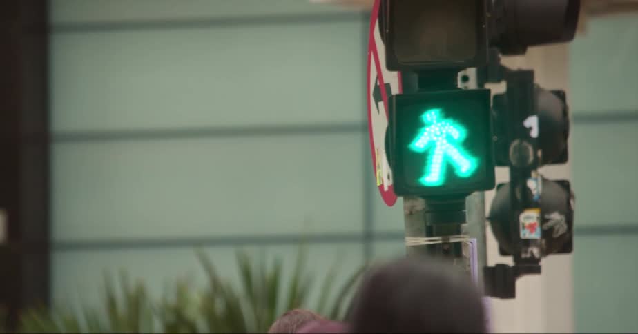 People walk across a city street with a pedestrian walk signal glowing green