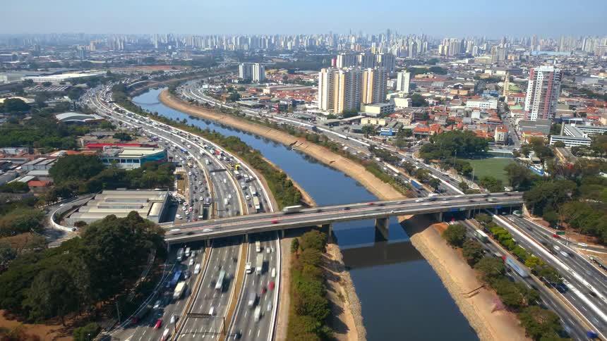 Aerial timelapse of cars and trucks travelling on the highways in a city with a river running between them on a sunny day