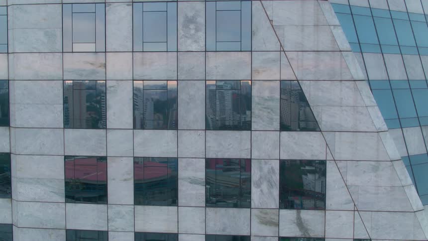 The side of an office building with other high rise buildings reflecting in the windows at dawn