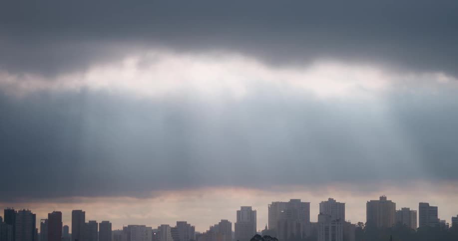 The sun shines through dark clouds on city buildings