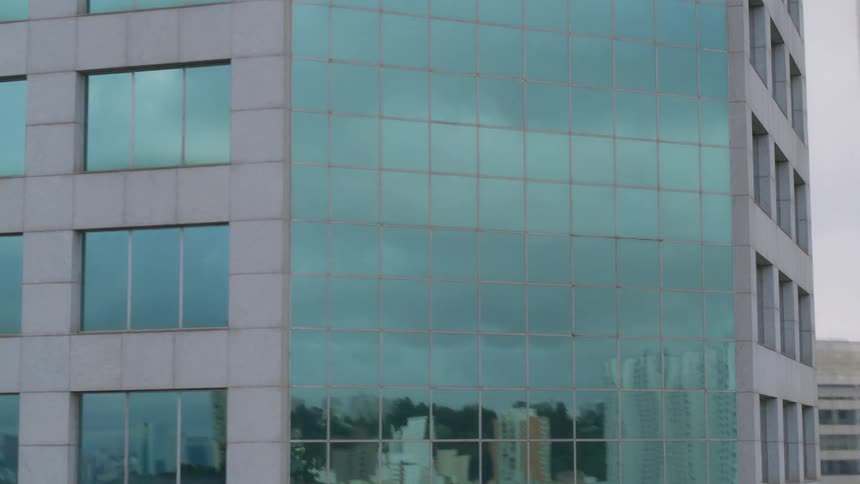 Reflection of trees and buildings in the windows of a tall building in the city as cars travel on the street below