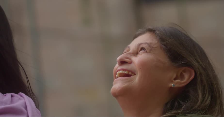 A woman smiling outside and putting her hand on her cheek