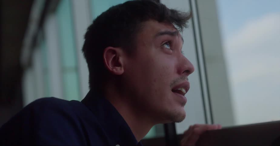 A man with a worried look on his face looks up at the sky through an office window