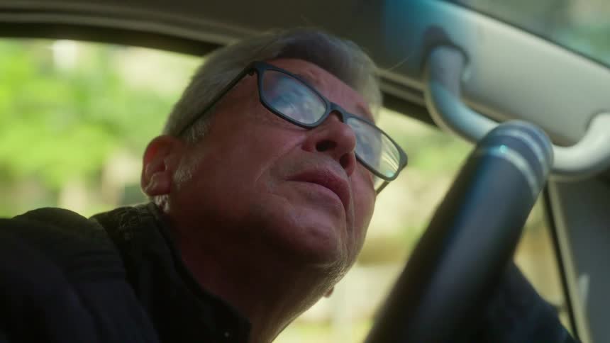 A man sits in his parked car and looks up
