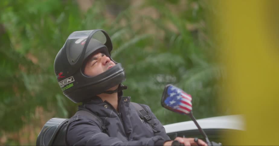 A man on a motorcycle beside a car looks up towards the sky