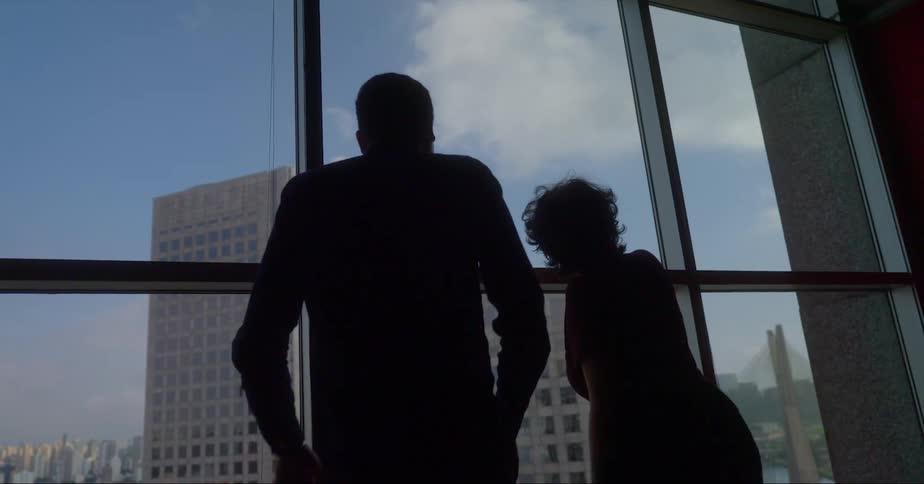 A man and woman walking up to a window looking at skyscrapers