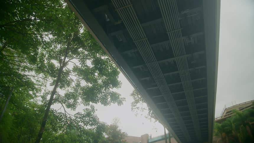 An overpass can be viewed from below as trees and buildings are located nearby
