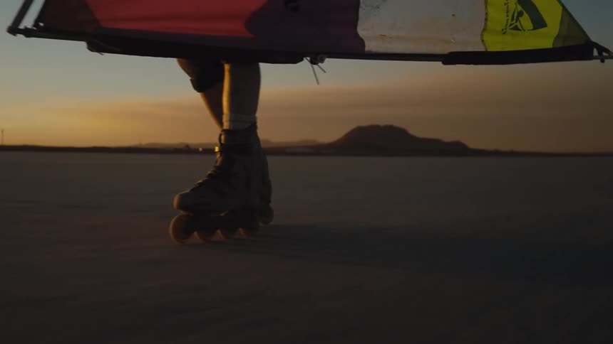A person wearing roller blades uses a handheld sail to cruise over the flat dusty ground