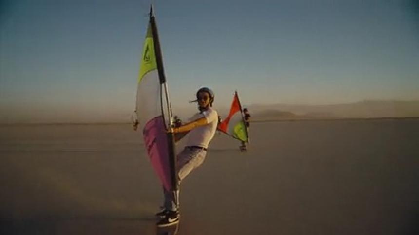 People windsurfing across a sandy desert