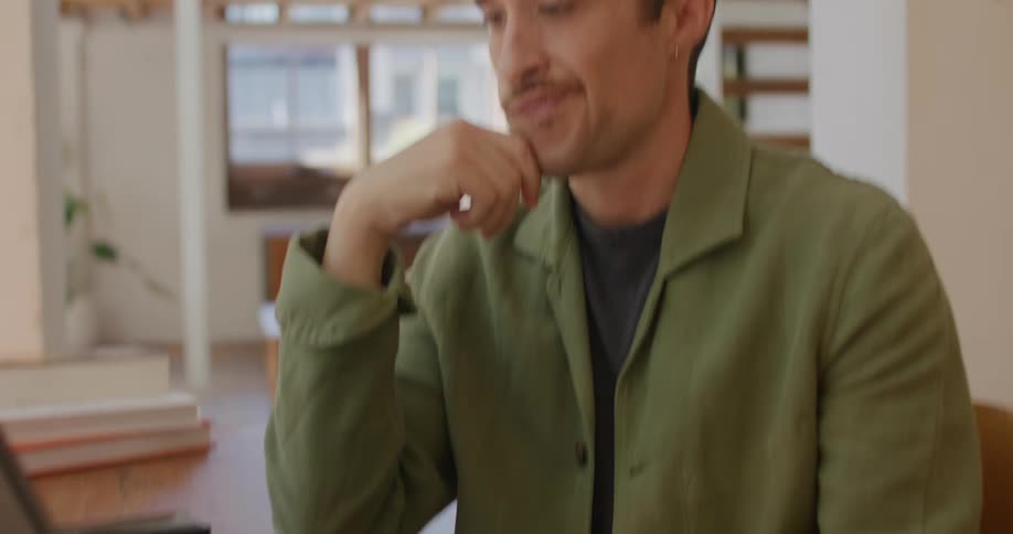 Man with mustache and green shirt sitting at table thinks and types on tablet keyboard