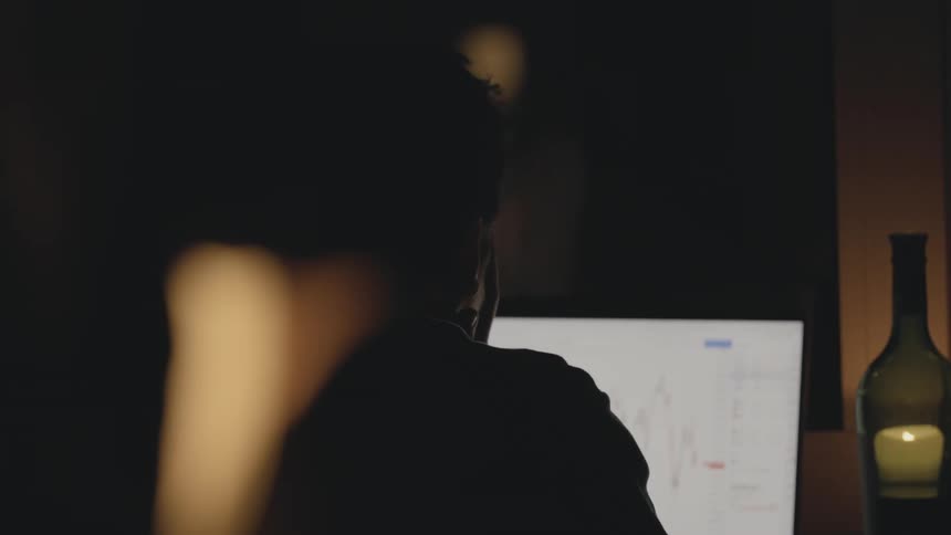 A man walks over to a computer screen and sits down to view stock market displayed on it
