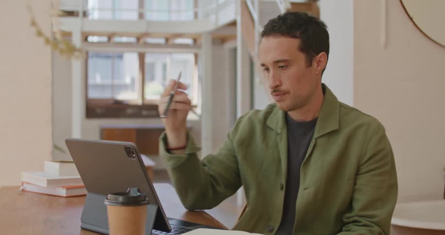 Man with mustache and green shirt works on tablet and writes down in notebook
