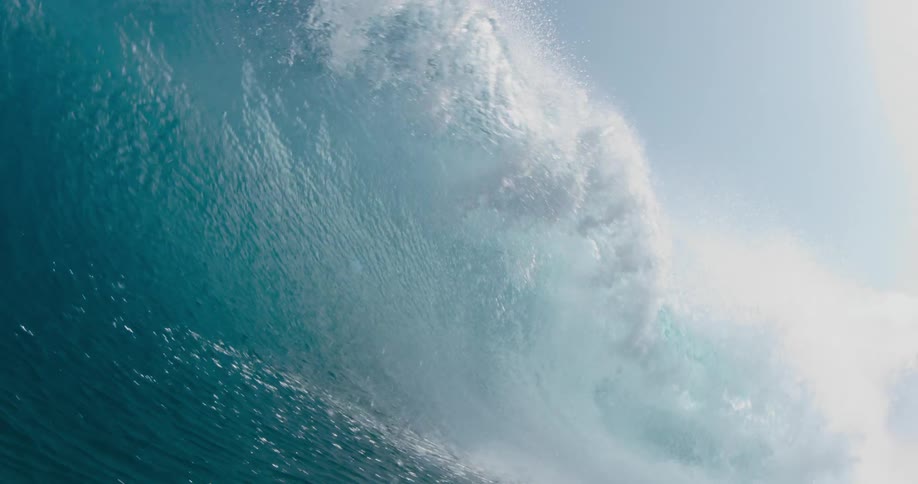 The sun shines on a big blue wave splashing as it rolls overhead
