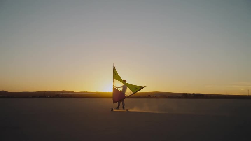 A man windsurfing across the desert at sunset